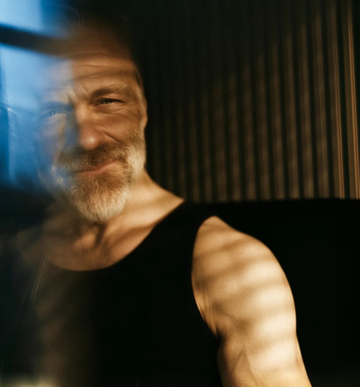 A smiling man in his fifties in warm window light, with Healthspan testosterone injection, enclomiphene and testosterone gel shown in front