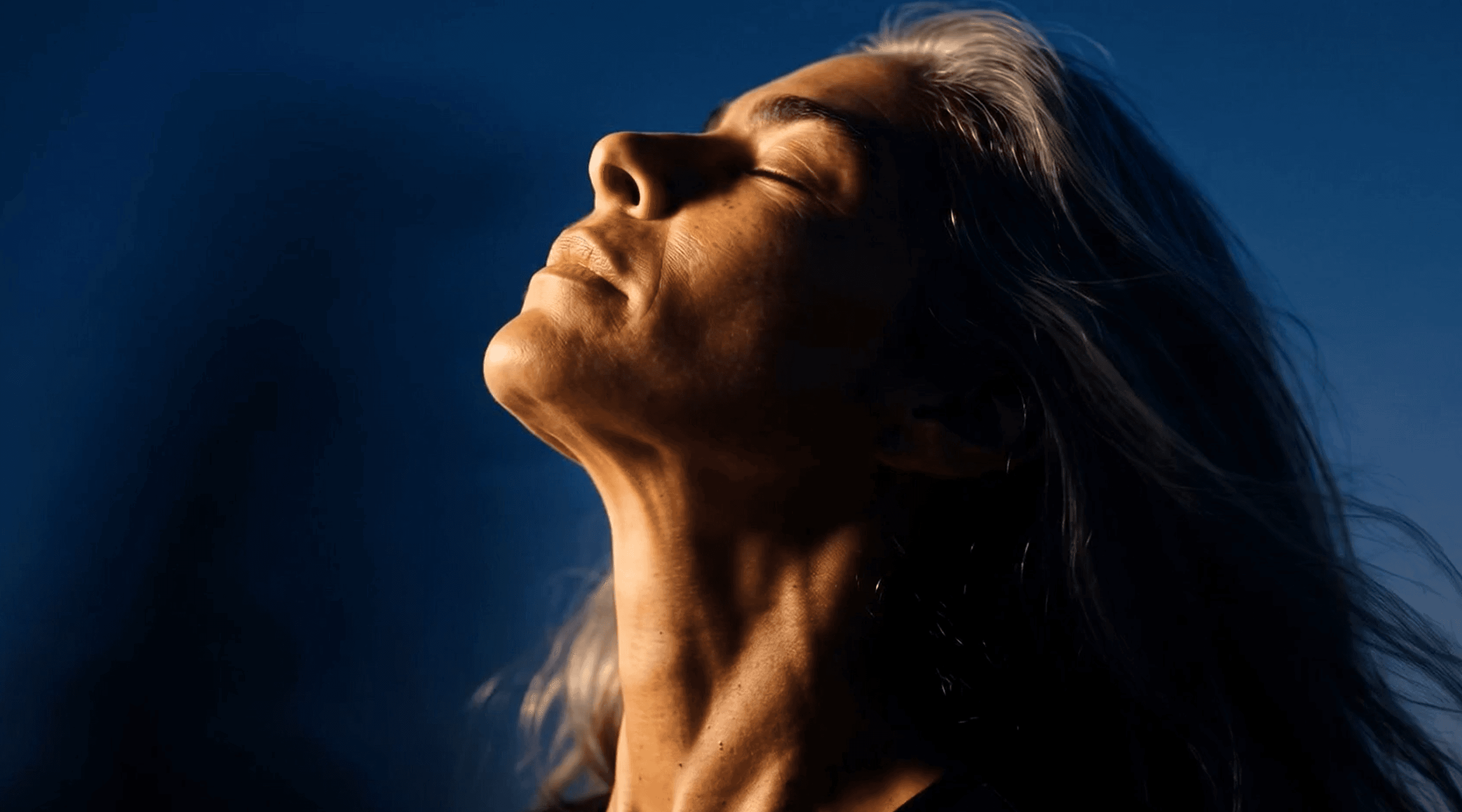 Portrait of a woman in her fifties, eyes closed, face lifted toward the sky.